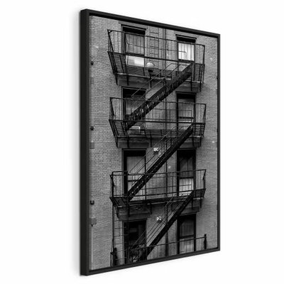 Emergency exit vertical – svart ram. Svarta räcken, brandtrappor och vilplan löper i diagonaler över en tegelklädd husfasad.