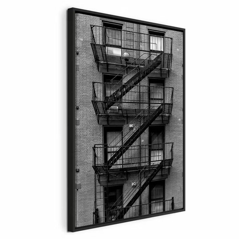 Emergency exit vertical – svart ram. Svarta räcken, brandtrappor och vilplan löper i diagonaler över en tegelklädd husfasad.
