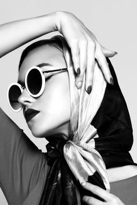 Stylish lady vertical – motivvy. En kvinna med ljus scarf och runda solglasögon håller en hand över huvudet i ett kontrastrikt svartvitt porträtt.