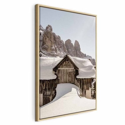 Winter in the dolomites – naturfärgad ram. En mörk trästuga ligger inbäddad i snö nedanför höga, klippiga bergstoppar.