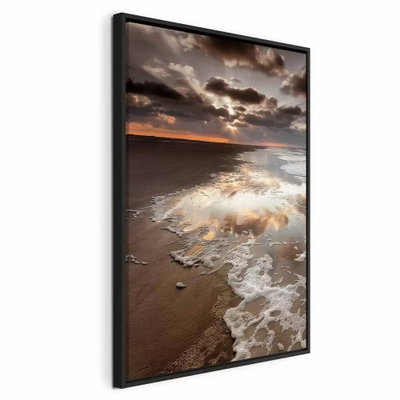 Present distraction vertical – svart ram. Vita vågor rullar in över en sandstrand under en dramatisk molnhimmel med ett smalt varmt ljus vid horisonten.