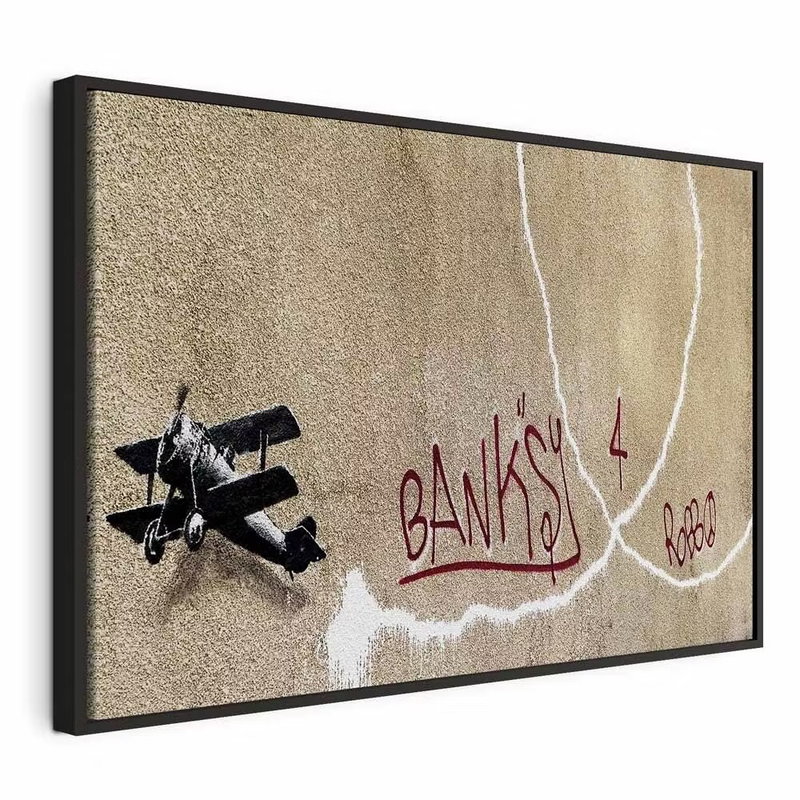 Banksy and s plane red – svart ram. Ett mörkt litet flygplan och långa vita rökspår omger röd handskriftsliknande text på en brungrå botten.