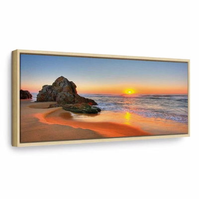 New day narrow – naturfärgad ram. Solen stiger över havet och färgar vågor och sand varmt orange kring en mörk klippa.