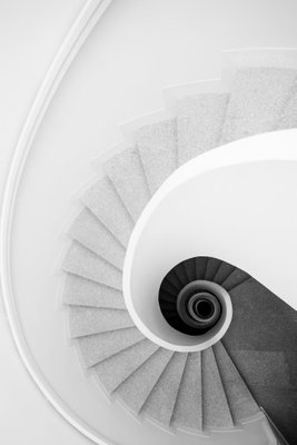 White stairs vertical – motivvy. En vit trappa vrider sig runt en mörk mittpunkt. Räcken och steg ger bilden ett tydligt geometriskt djup.