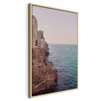 Turquoise coast vertical – naturfärgad ram. Stenbyggnader ligger på en klippkant ovanför turkost vatten, under en ljus himmel.