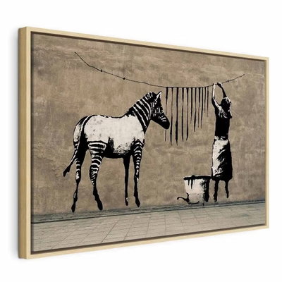 Banksy washing zebra on – naturfärgad ram. En zebra står intill en person som hänger mörka ränder på en tvättlina i ett svartvitt väggmotiv.