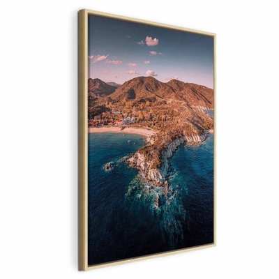 Cliff in kalamitsi vertical – naturfärgad ram. En bergig kust med varma brunorange klippor skjuter ut i ett djupt blått hav under en ljus kvällshimmel.