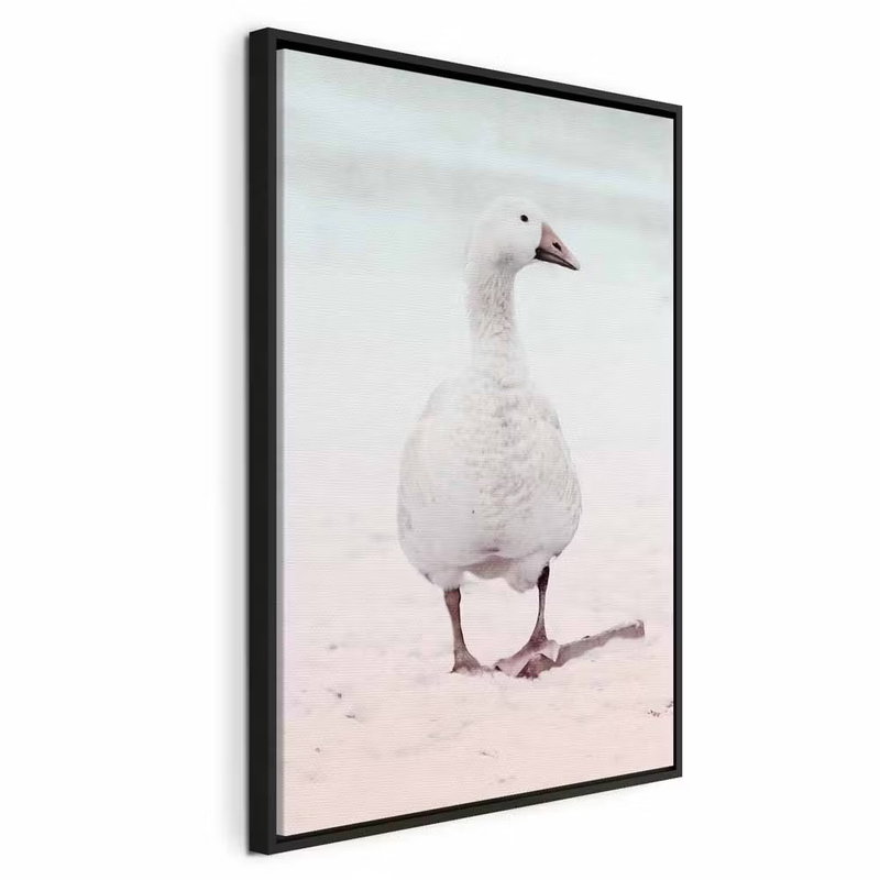 Winter duck vertical – svart ram. En vit vattenfågel står i ett ljust vintermotiv med blekt rosa och blå toner.