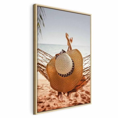 Hammock on the beach – naturfärgad ram. En stor stråhatt ligger framför uppsträckta ben i en hängmatta över en varm sandstrand.