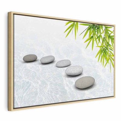 Stone peace wide – naturfärgad ram. En rad släta grå stenar ligger på en ljus yta med gröna bambublad i bildens ena hörn.