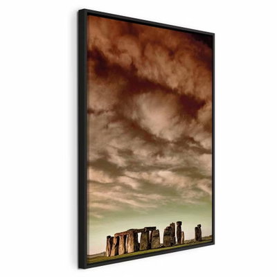 Clouds over stonehenge – svart ram. En rad stora, mörka stenar står längs en låg horisont under en vid bruntonad molnhimmel.
